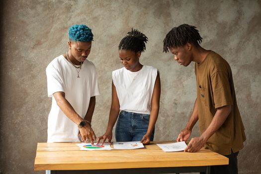 Three young adults engage in a creative project planning session, examining documents together.