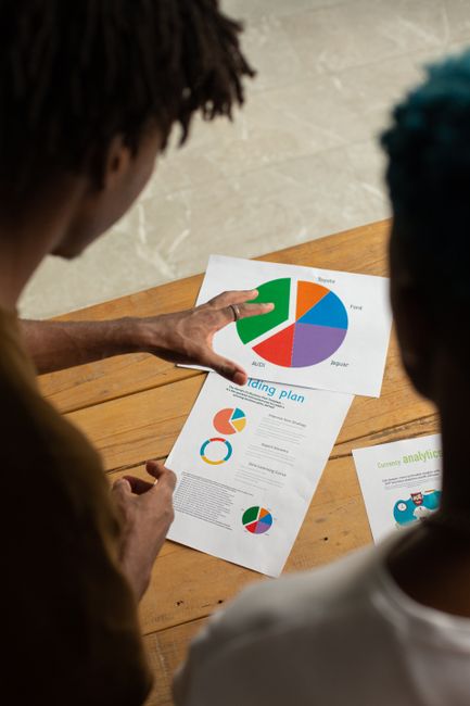 From above of crop anonymous African American males standing near table and discussing diagram together while working on project - How to Create Custom Infographics That Naturally Attract Links