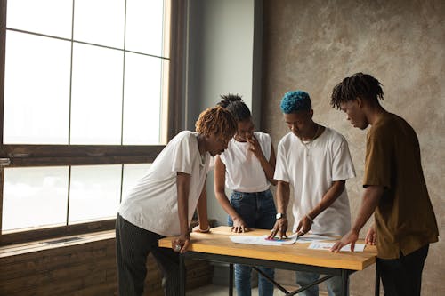 Free Group of young African American entrepreneurs in casual clothes gathering around table and analyzing details of project together while working with documents Stock Photo