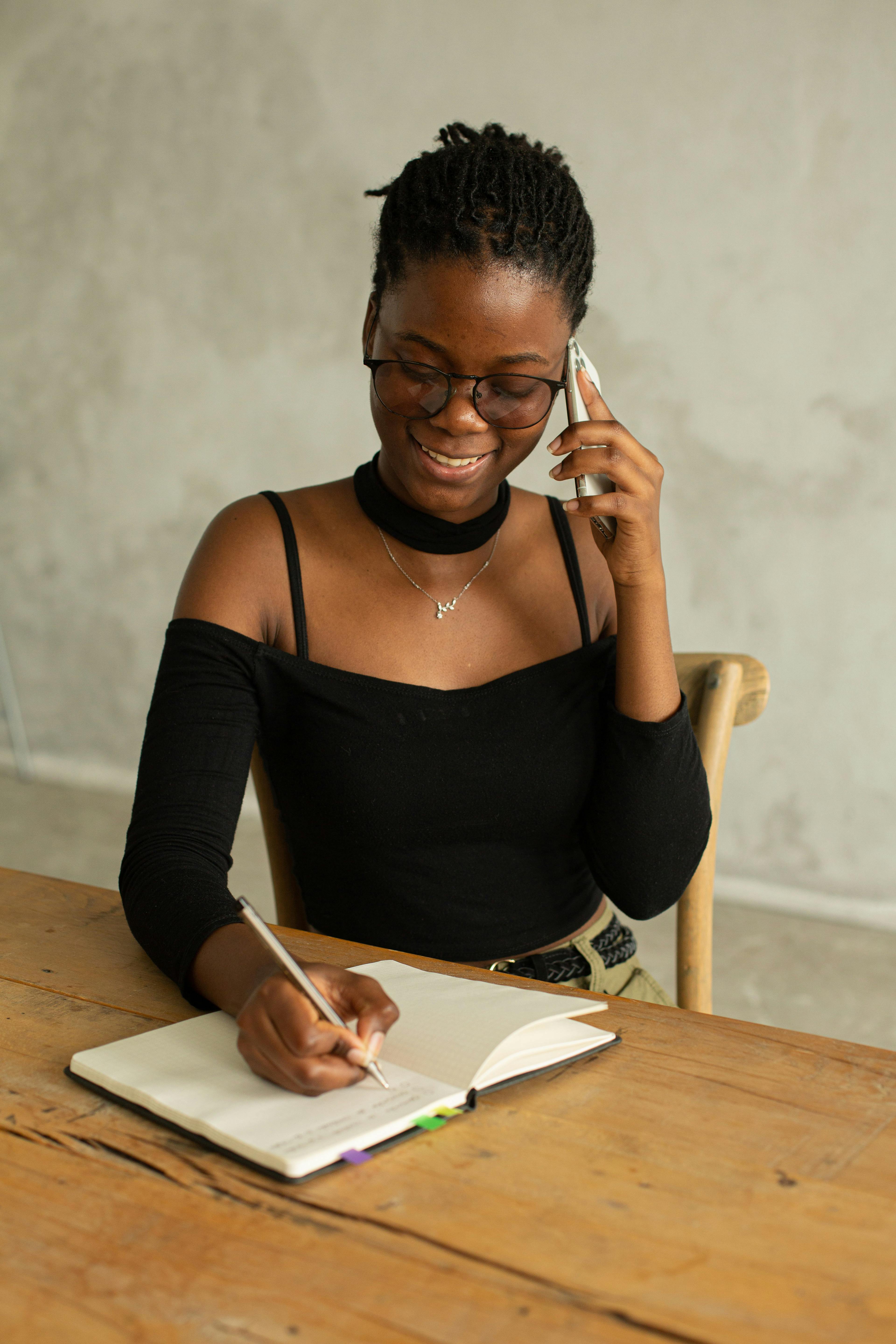 smiling black woman writing notes during phone call