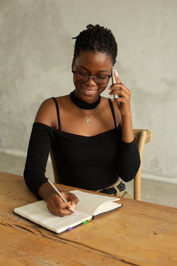 Smiling Black Woman Writing Notes During Phone Call