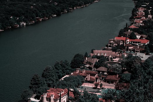 Aerial view of elegant homes along a tranquil river surrounded by lush greenery, showcasing affluence and scenic beauty.