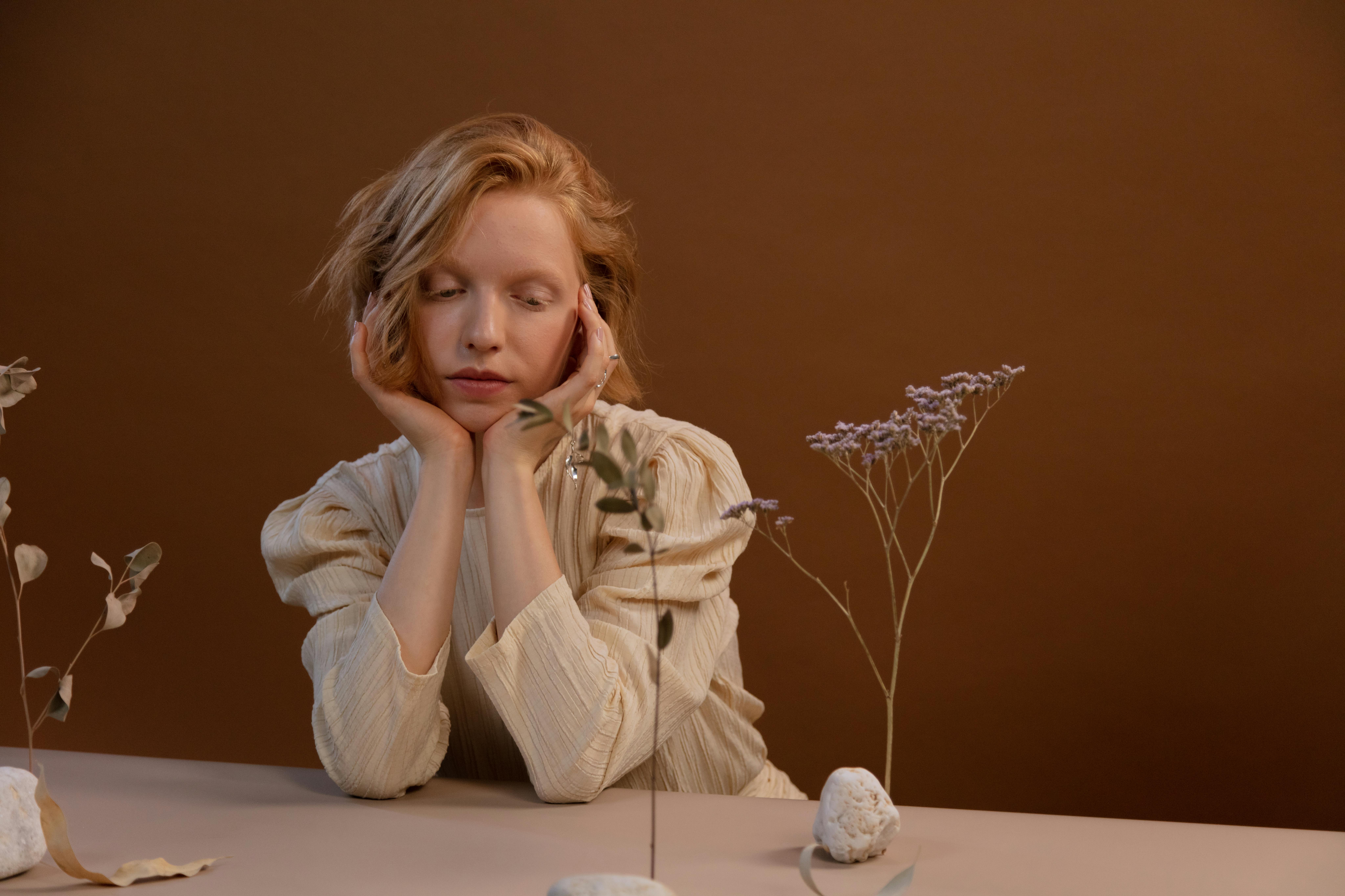 Woman in a contemplative pose with dried flowers on a warm brown backdrop.