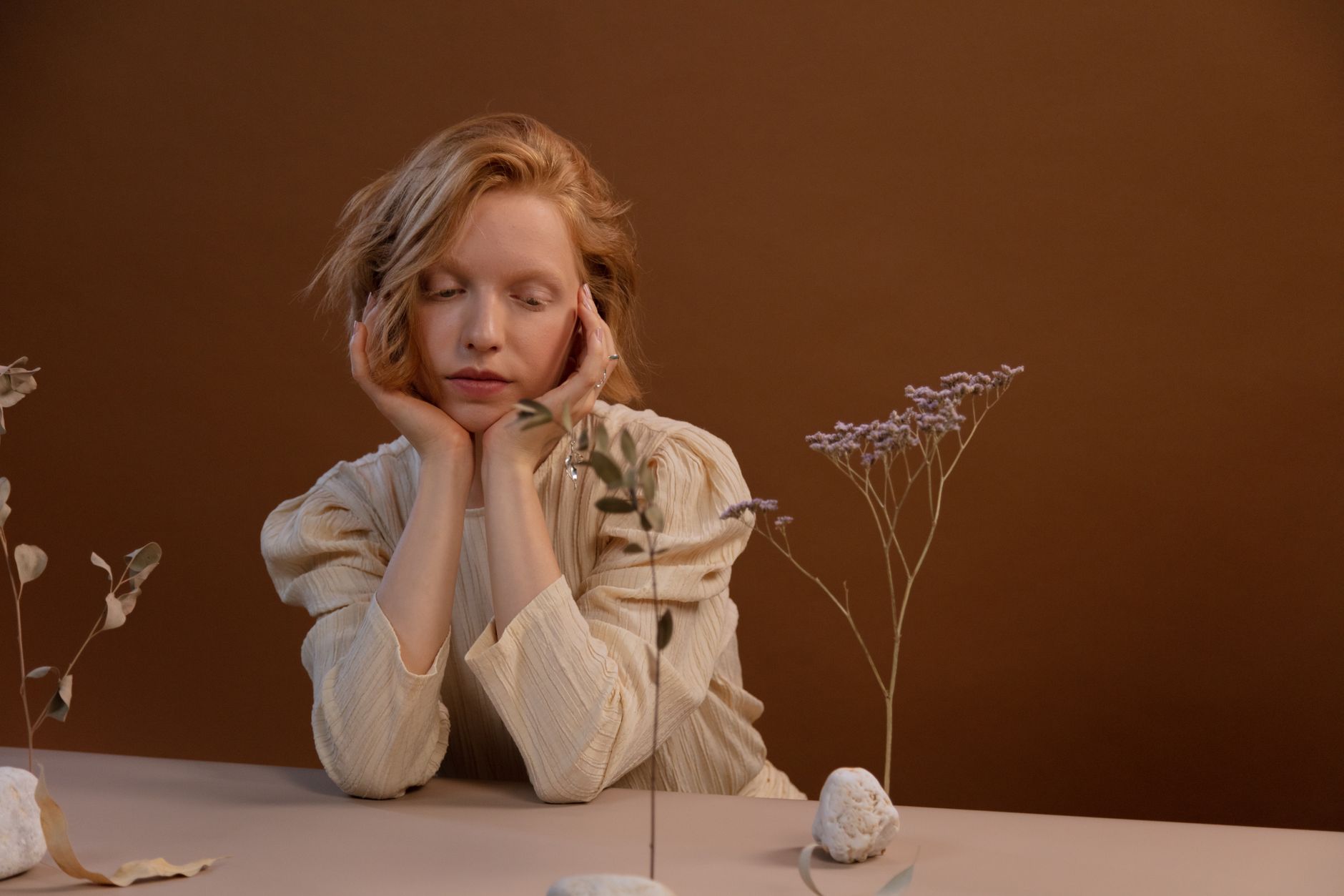 Woman in a contemplative pose with dried flowers on a warm brown backdrop.