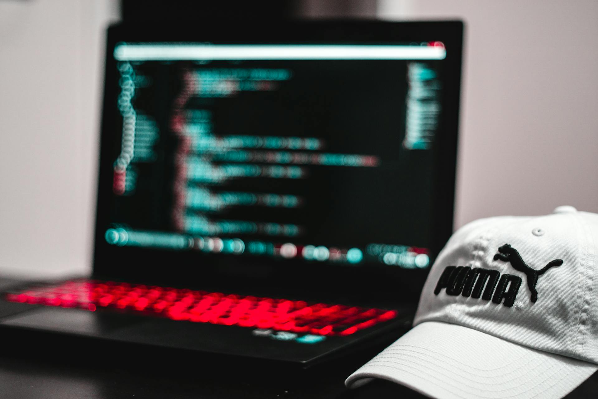 Blurred laptop screen displaying code with a white cap in focus, depicting a tech workspace.