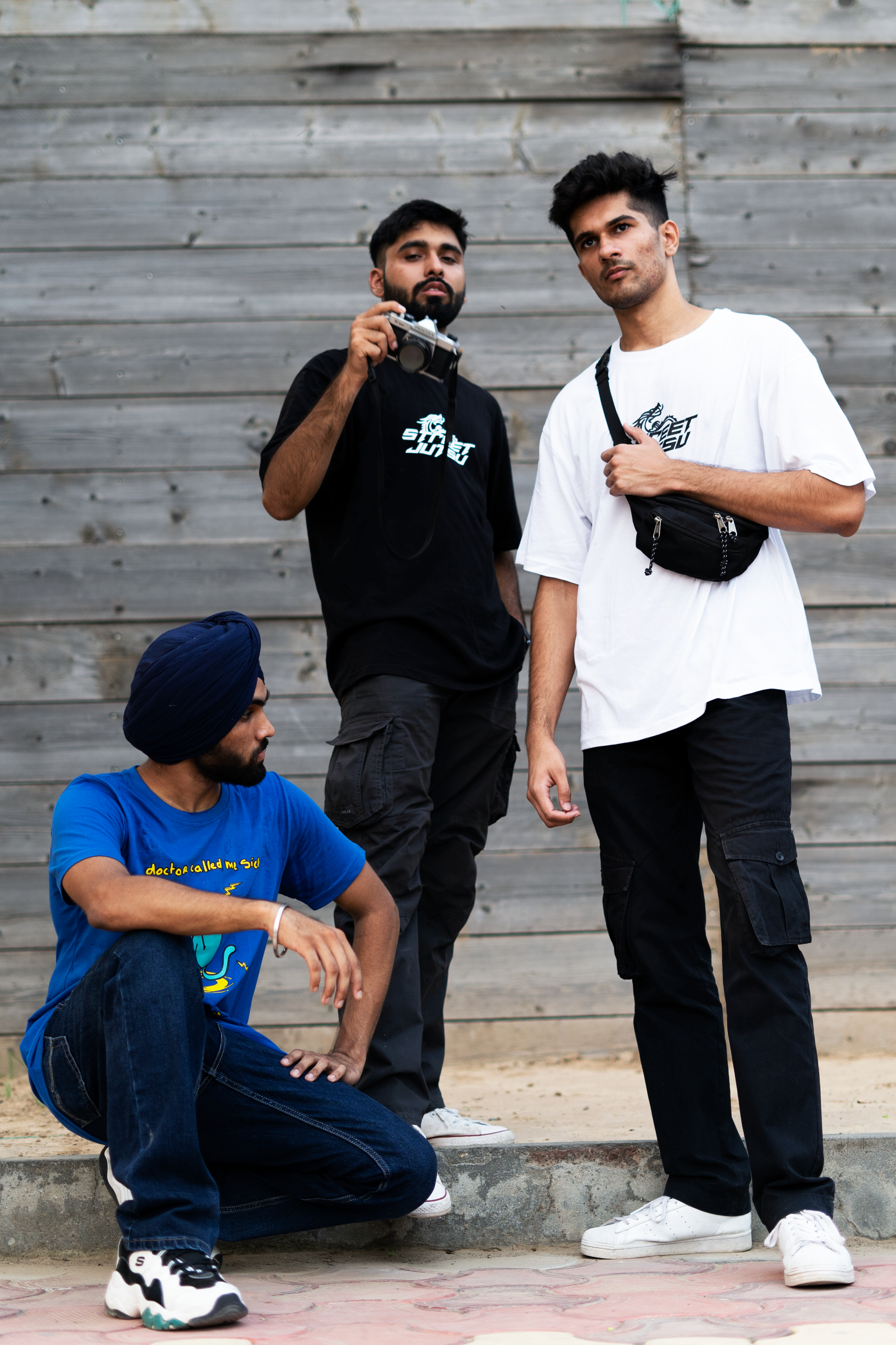Three fully clothed male streetwear models posing in an outdoor urban setting