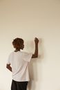 Back view of anonymous African American young male with dreadlocks in white t shirt writing on white wall