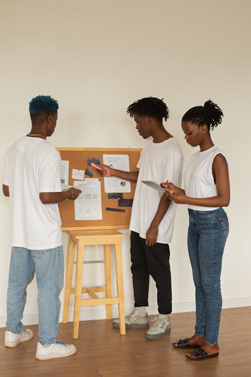 Side view of full body young African American students standing near whiteboard and examining documents