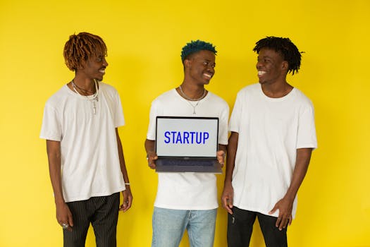 Three smiling young men in casual attire displaying a laptop that says 'Startup' on a vibrant yellow background.