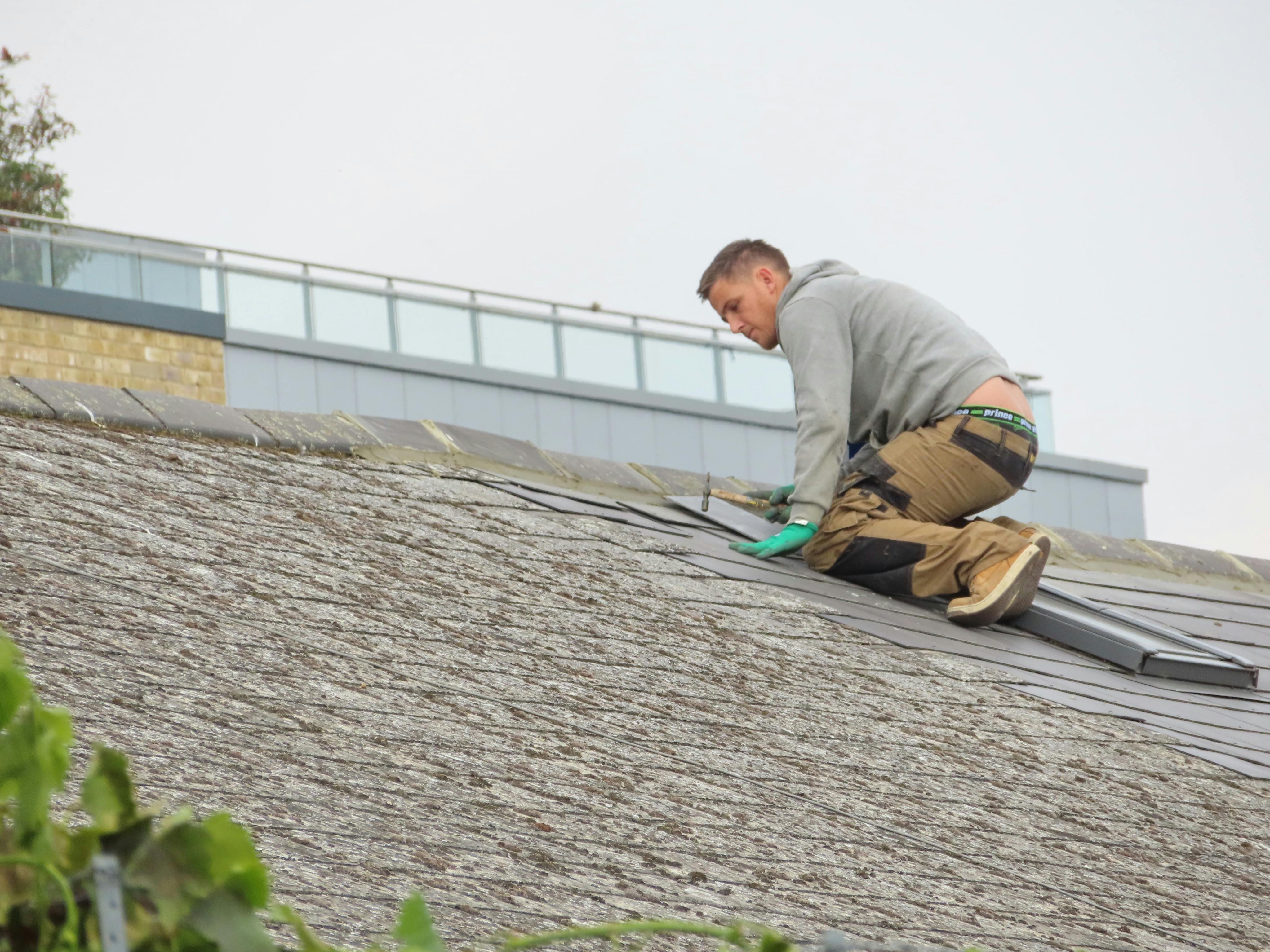 Construction worker installing shingles on a rooftop. Outdoor building maintenance.