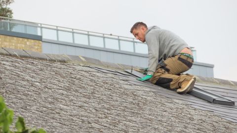 Construction worker installing shingles on a rooftop. Outdoor building maintenance.