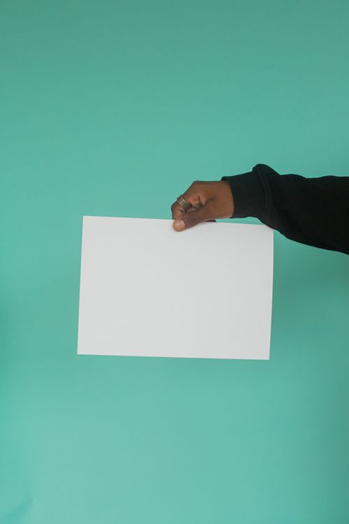 Free A hand holding a blank sheet of paper on a turquoise background, ideal for mockup presentations. Stock Photo