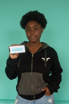 African American woman with afro hair holding a smartphone displaying 'Business'.