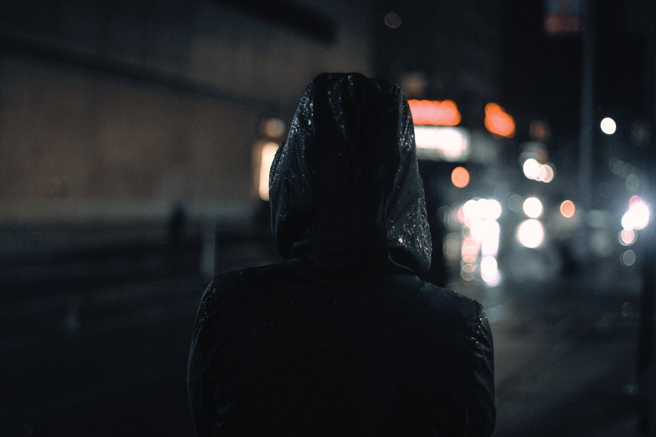 back view of a hooded person in the city at night navigating wet stree