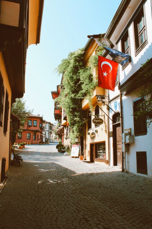 Free Picturesque alley in Turkey featuring vibrant buildings and Turkish flag under clear blue sky. Stock Photo
