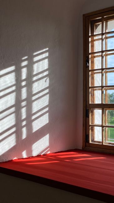 Minimalist interior with sunlight casting shadows through a wooden window onto a red sill.