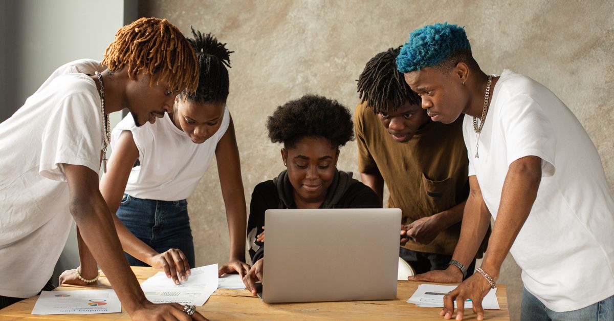 A diverse group of young adults collaborating on a laptop in an indoor workspace.