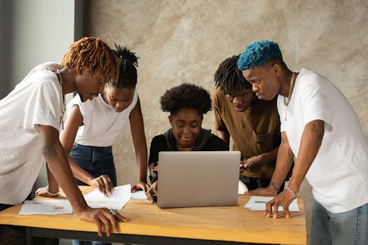 A diverse group of young adults collaborating on a laptop in an indoor workspace.