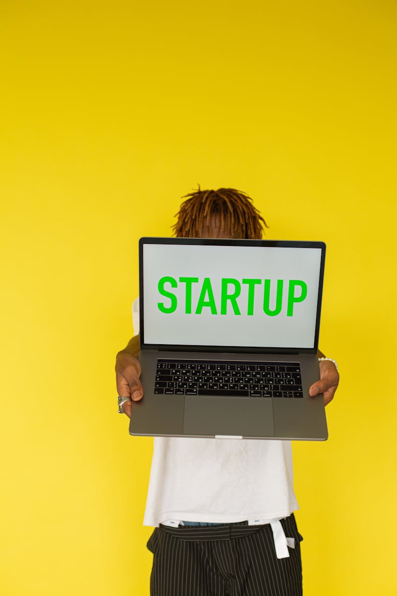 Person holding a laptop with 'STARTUP' on the screen against a yellow background