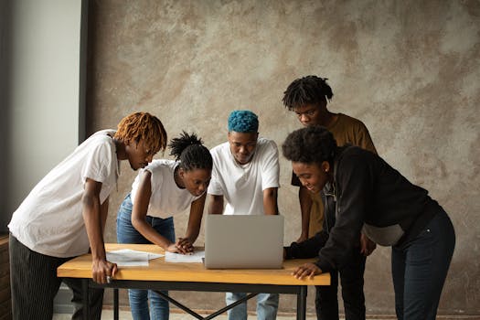 A group of young adults collaborate around a laptop, conveying teamwork and innovation indoors.