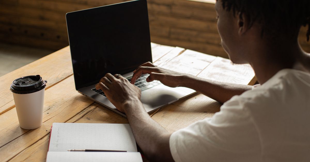 person typing on laptop with coffee cup and open Bible