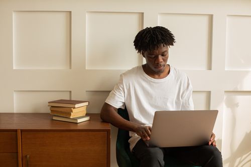 Free A young man focused on his laptop, sitting in a modern home setting with books on the table. Stock Photo