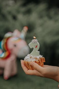 Hand holding a cupcake with a number 2 candle outdoors with a unicorn backdrop.