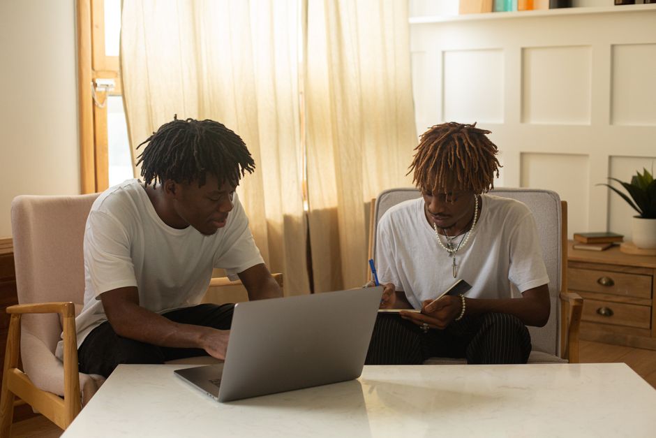 Two young men working together at home, discussing ideas and using a laptop. Two young men working together at home, discussing ideas and using a laptop.