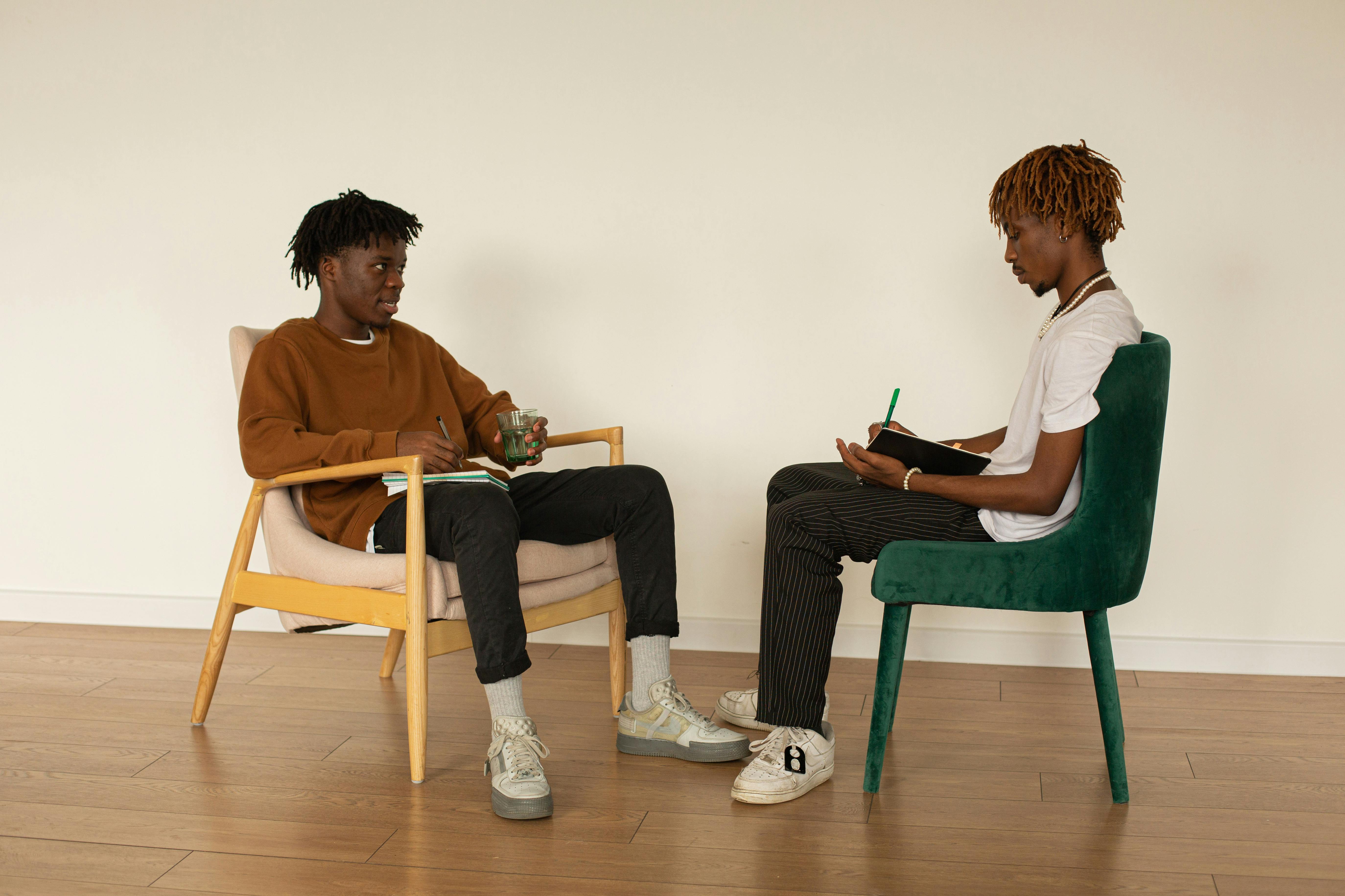 Two young men discussing ideas over notebooks indoors, engaging in creative collaboration.