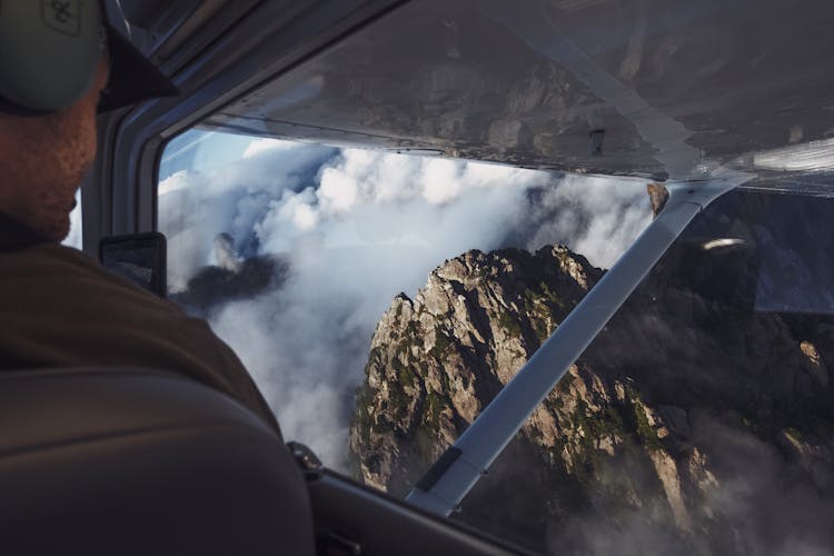 Man In Aircraft Looking At Rocky Mountain In Clouds