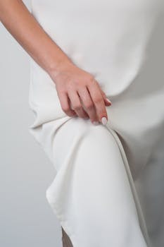 Close-up of a woman's hand resting gracefully on white silk fabric, showcasing elegance.