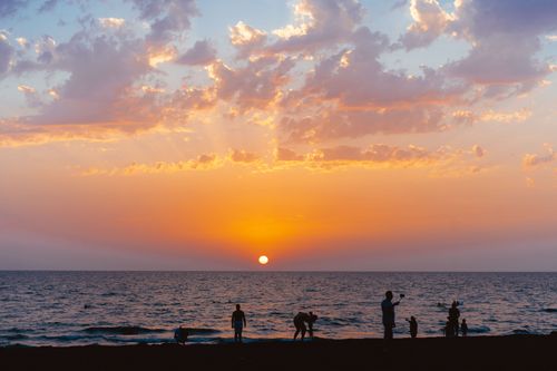 Free Stunning beach sunset with silhouettes of people and vibrant sky colors. Stock Photo