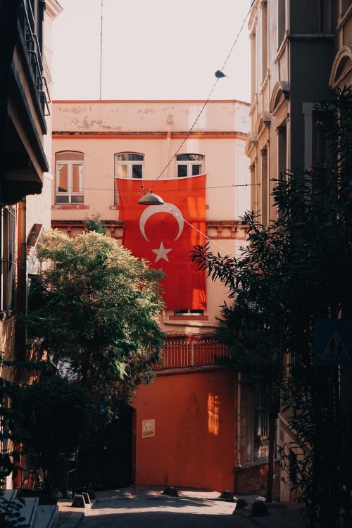 Free Turkish flag hanging on a historic building facade in a sunlit alley, Istanbul. Stock Photo