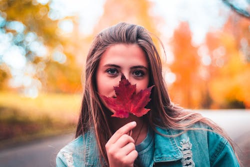 Selective Focus Photo of a Woman Holding a Red Maple Leaf