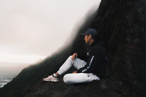 Free Man in Black Hoodie and White Pants Sitting on Rock Stock Photo
