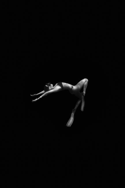 Black and white image of a ballet dancer elegantly posed against black background.