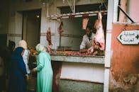 在一个热闹的户外市场，屠夫正在肉摊为顾客服务