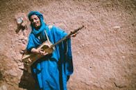 一位身着鲜艳蓝色服装的摩洛哥音乐家靠在乡村墙壁上，演奏着传统乐器