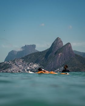 Surfers paddle on the waves with Rio de Janeiro's Two Brothers Mountain in the background.