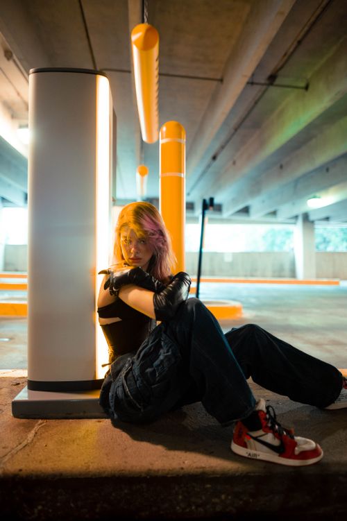 Free Stylish young woman with colored hair posing in an urban parking setting, wearing trendy attire. Stock Photo