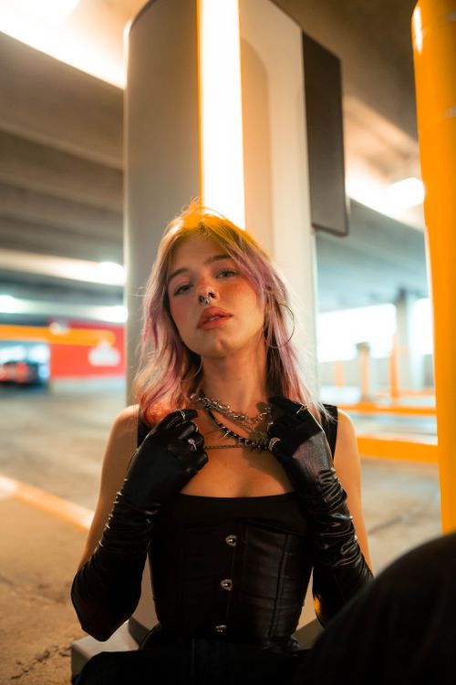 Free Confident woman in black corset and gloves poses in a vibrant parking garage. Stock Photo
