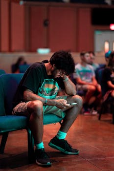 A man focused on his smartphone while sitting in an auditorium setting.
