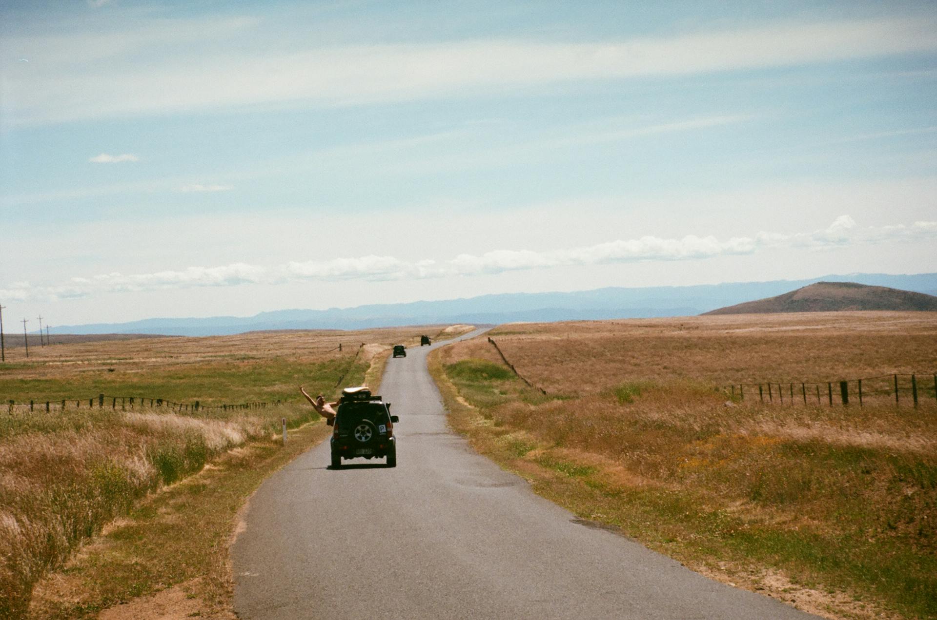 A serene countryside road with vehicles under a bright blue sky, perfect for travel themes.