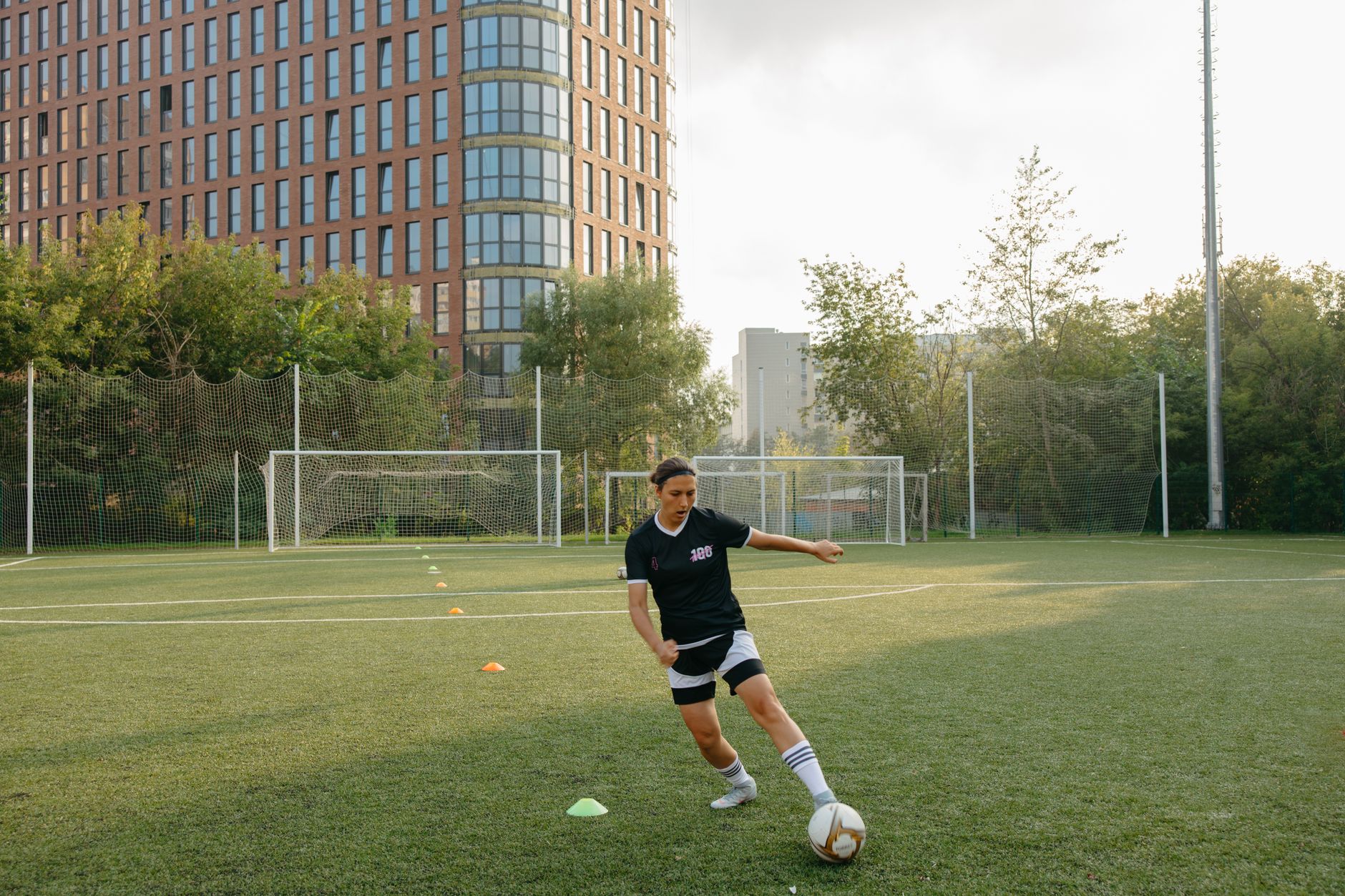 A woman practicing soccer skills on a city field with tall buildings in the background.