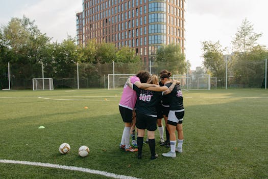 Female soccer players in a huddle on a grass soccer field, preparing for a match.