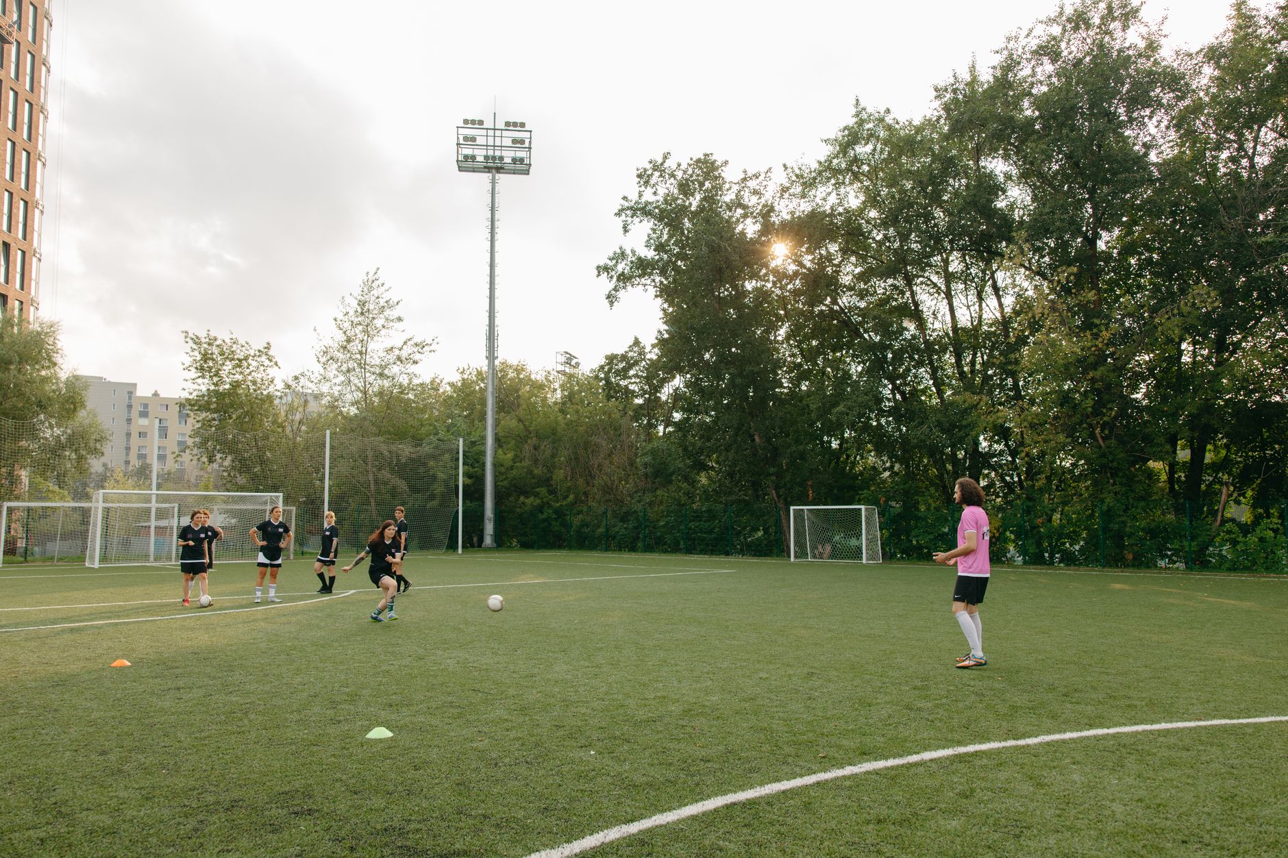 women’s football team practicing cutback finishes inside a marked penalty area under evening floodlights