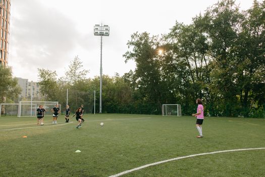 Women's soccer team practicing on an outdoor field, guided by a coach under a bright sun.