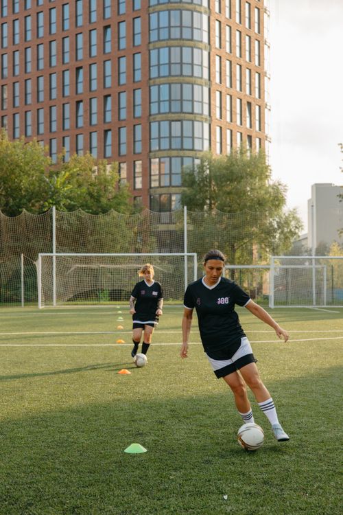 Free Two women training in soccer uniforms on a city field during daylight. Stock Photo