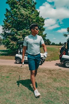 Male golfer in sunglasses walking across a sunny golf course with golf carts in Oklahoma City.