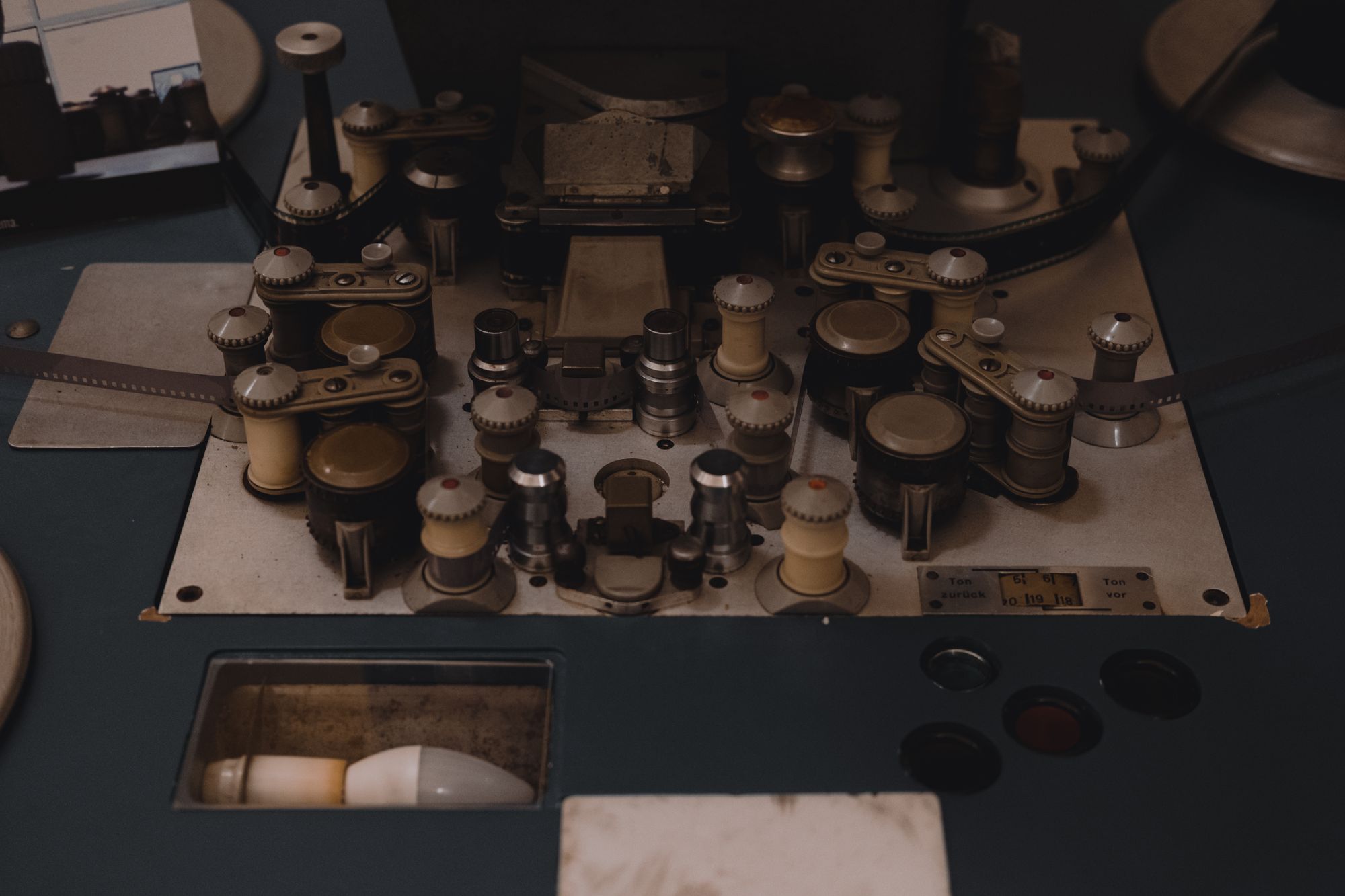 A vintage film-production cutting table, film threaded through its brass rollers and sprockets under a work lamp